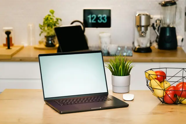 Robot camera frame ep03_step-040: a laptop, potted plant, mouse, and fruit basket on a kitchen counter, with a tablet, clock, kettle, and coffee machine behind them.